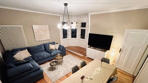 Un salon moderne avec un canapé bleu, une table à manger avec des chaises, un téléviseur et un lustre.