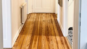 Un couloir doté d’un plancher en bois, d’une porte blanche avec des panneaux de verre et d’un luminaire au plafond.