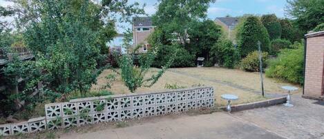 Un jardin arrière aménagé, avec une terrasse dallée, une clôture décorative et une variété d’arbres et d’arbustes.