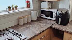 A kitchen with a gas stove, a microwave, a toaster, and a coffee maker. There are three small potted plants on the windowsill. - The Croft House Near Birmingham Airport and Nec (Birmingham)