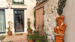 Une cour avec un chemin en briques, des plantes en pot, une porte et une statue.
