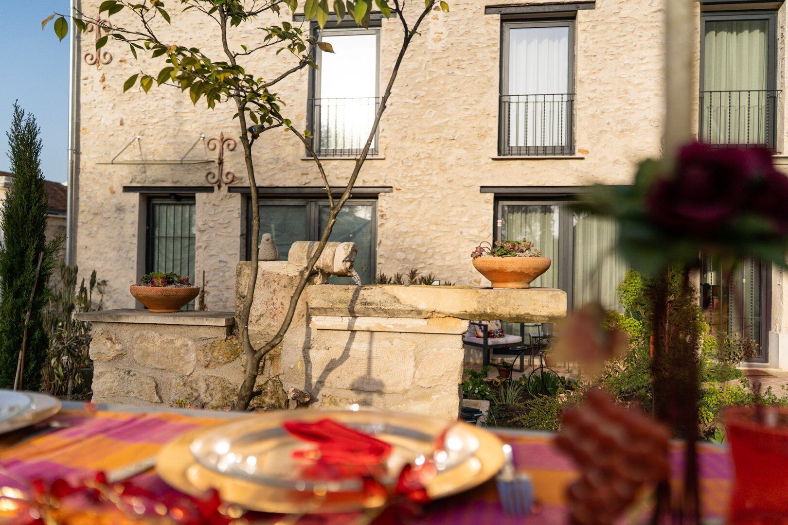 A stone building with multiple windows and balconies, a small outdoor seating area with a table set for dining, and potted plants.