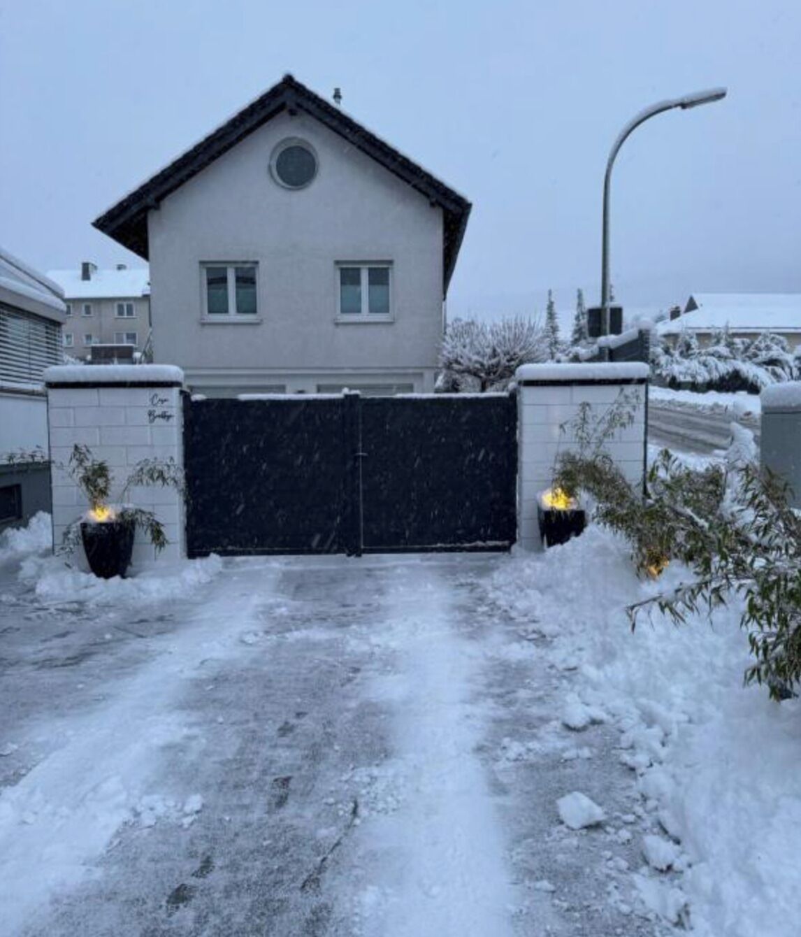 Un edificio residencial con una verja negra, rodeado de nieve y plantas.