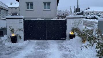 Un edificio residencial con una verja negra, rodeado de nieve y plantas.