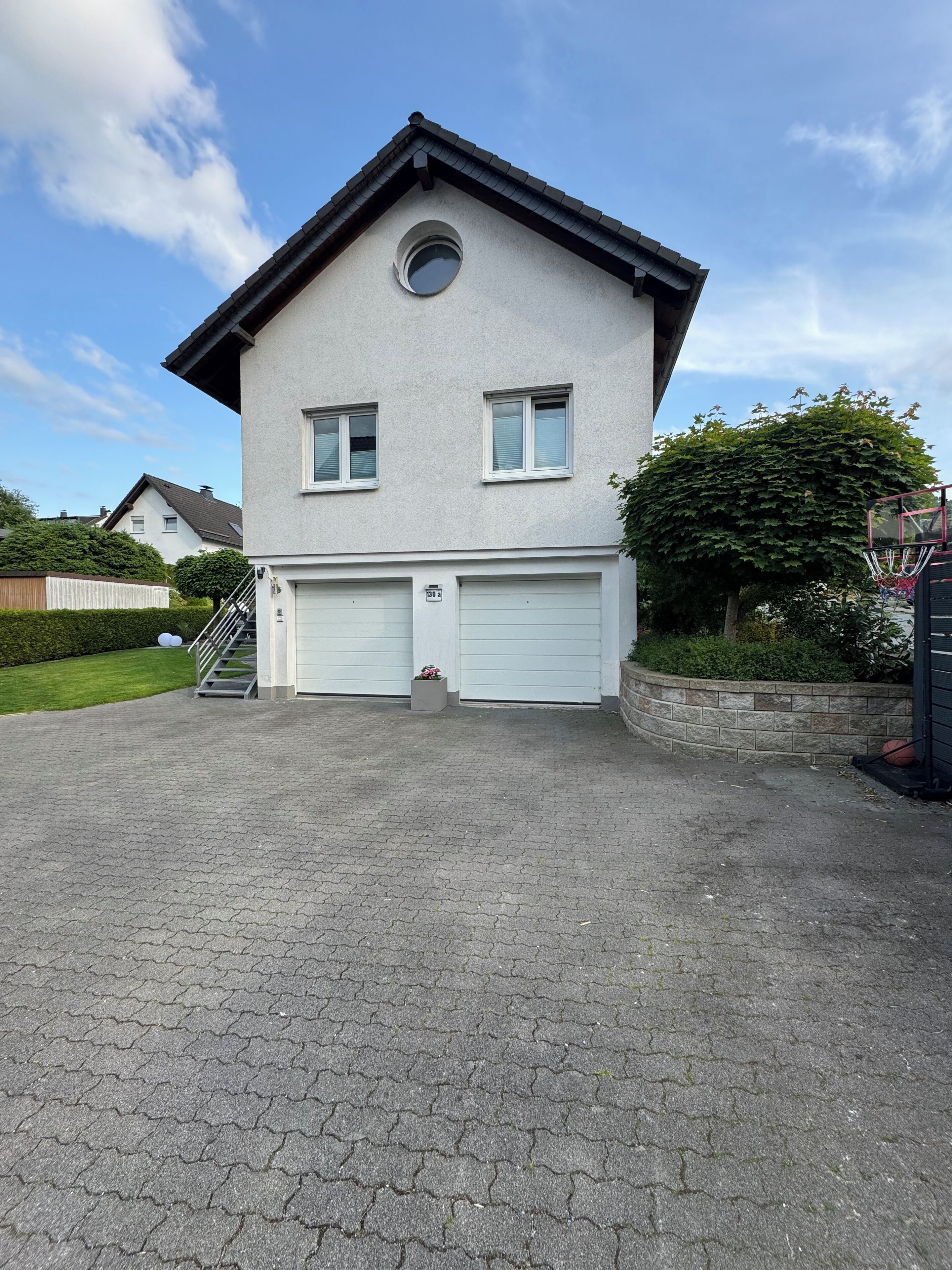Une maison à deux étages avec un garage, une petite fenêtre ronde et une allée pavée en briques.
