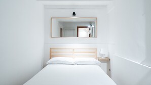 A minimalist hotel room with a single bed, a nightstand, a mirror, and a wall-mounted light fixture. - Meta Apartment by Wonderful Italy (Bari)
