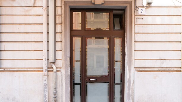 A brown double door with glass panels, a number '7' sign, and a white building facade. - Meta Apartment by Wonderful Italy (Bari)