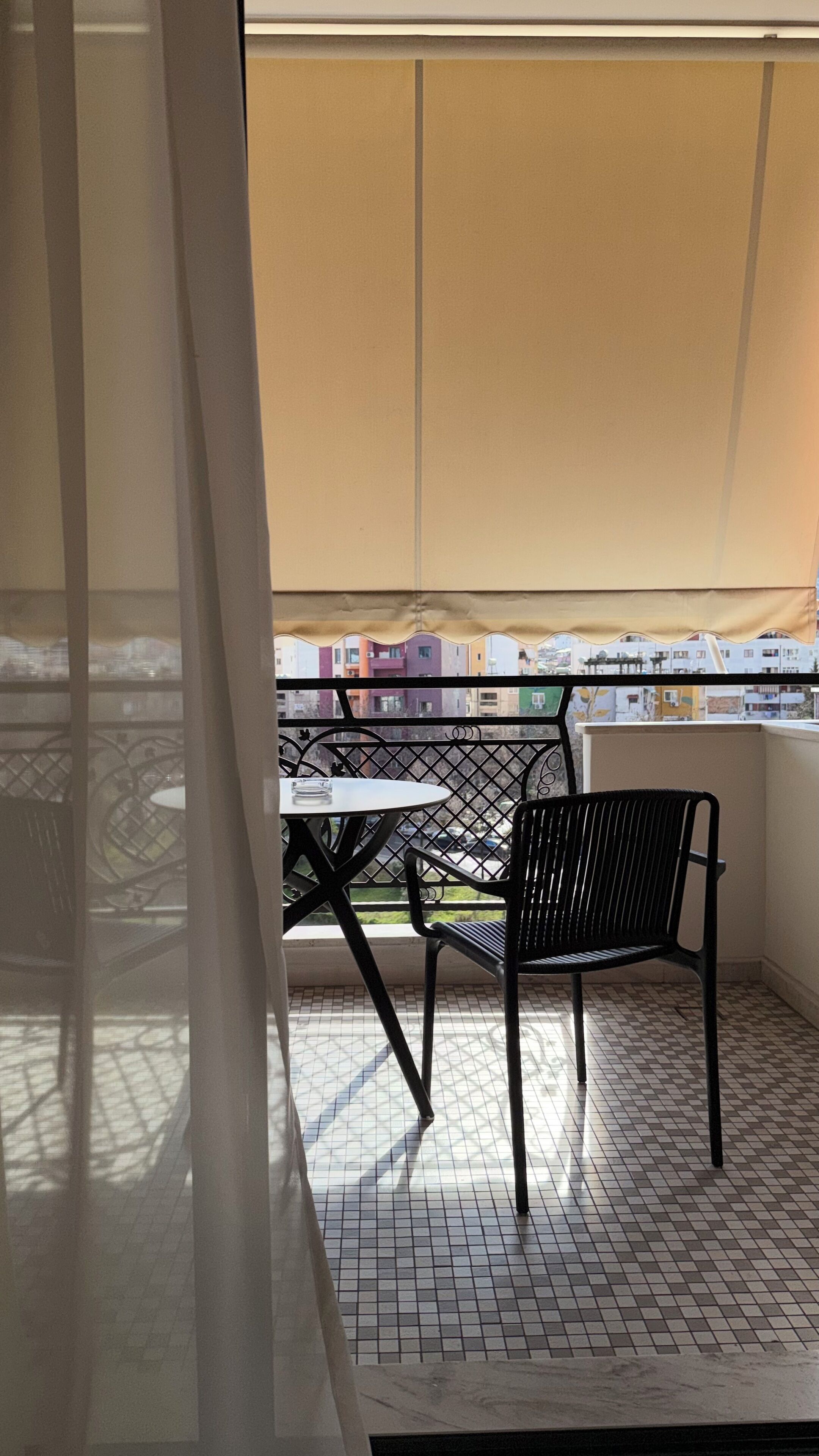 A balcony with a table and chairs, a view of buildings, and a tiled floor.