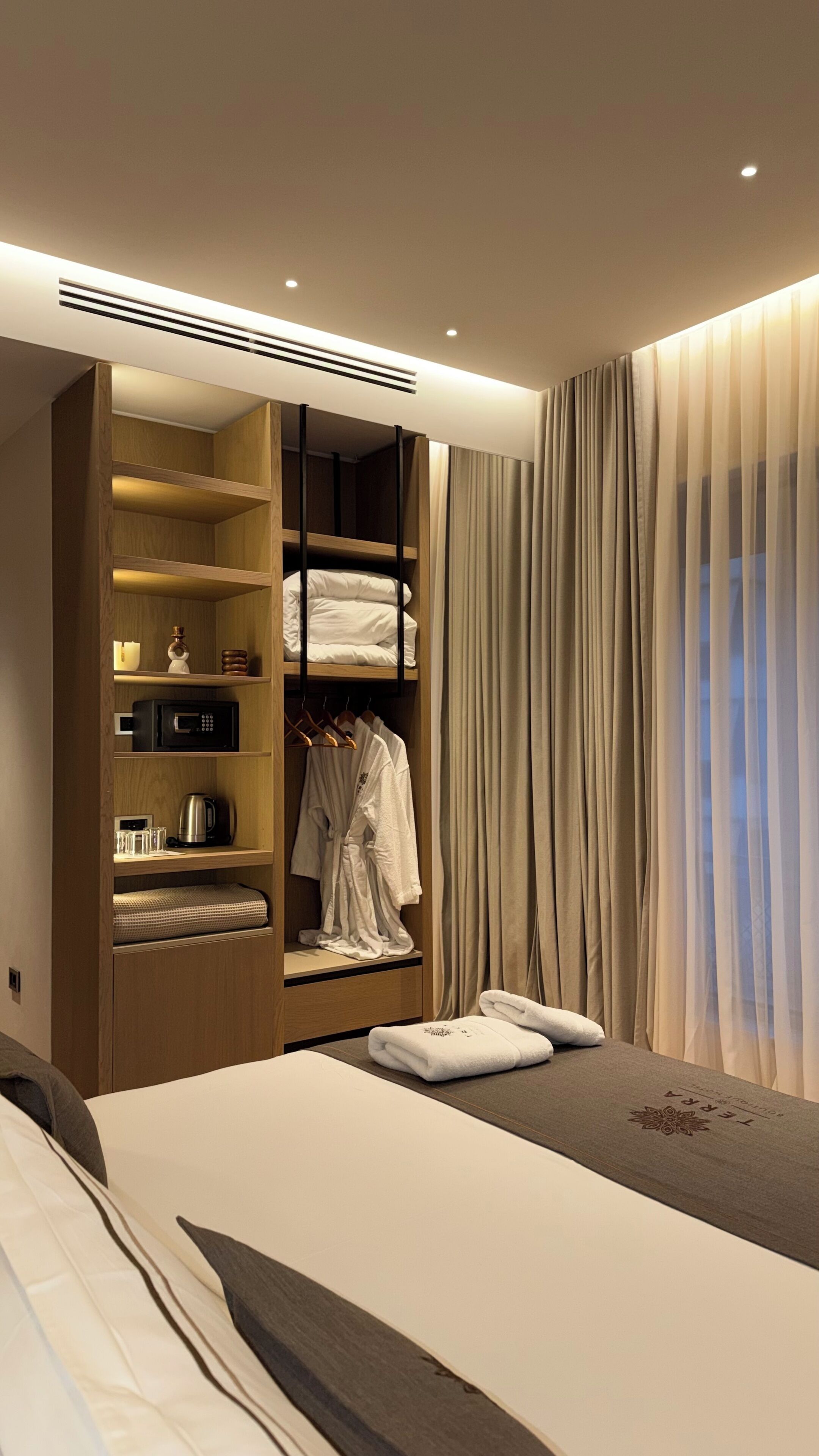 Una habitación de hotel moderna con una cama, un armario con estantes, un microondas y una tetera.