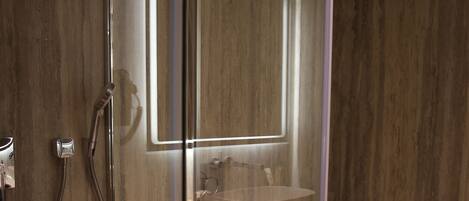 A modern bathroom with a glass-enclosed shower, a toilet, a bidet, and a mirror with integrated lighting.