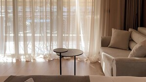 A hotel room with a bed, a small table, a sofa, and sheer curtains.