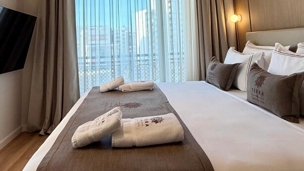 A hotel room with a large bed, a flat-screen TV, a city view, and a ceiling light.