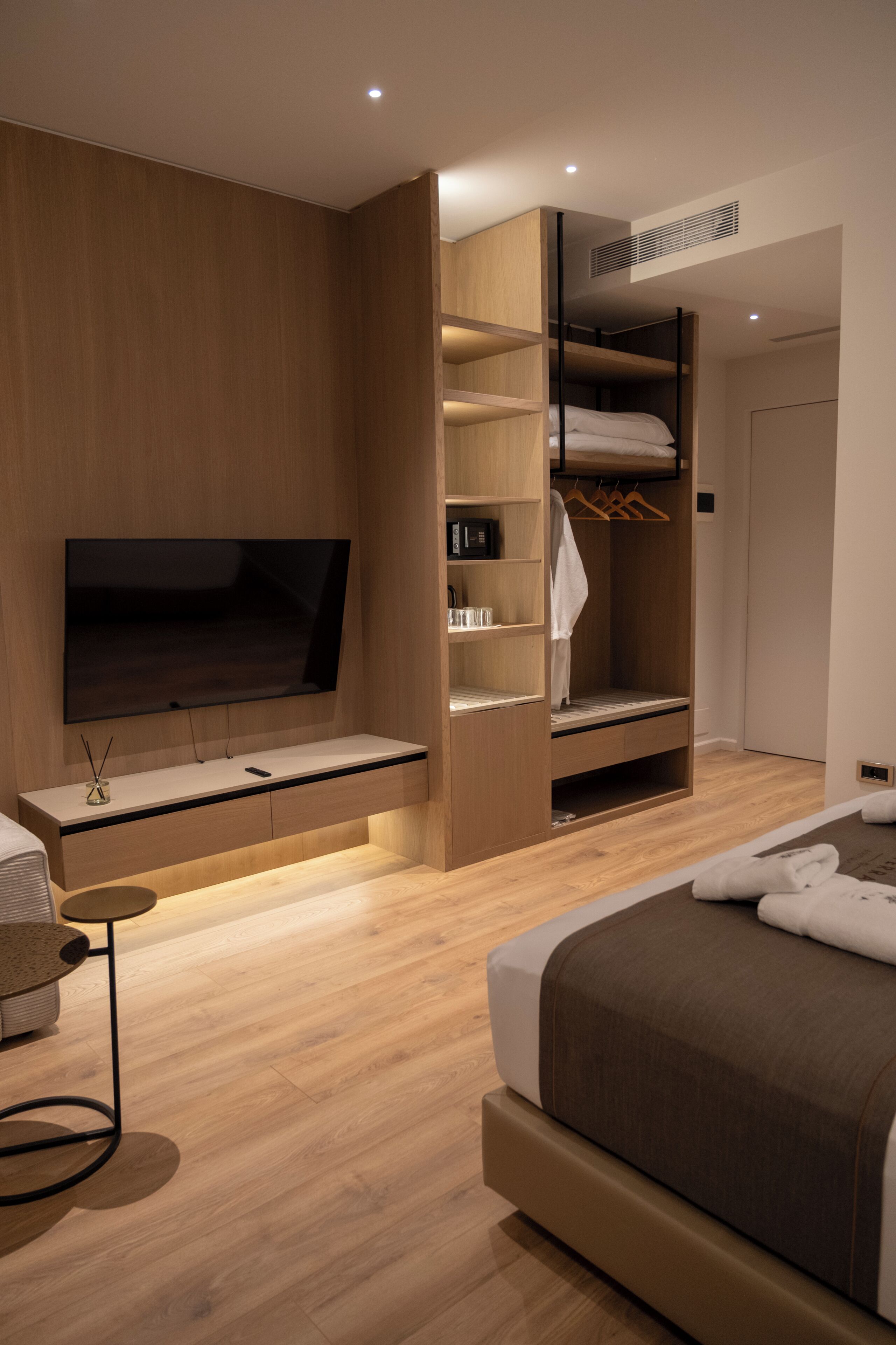 Habitació d'hotel moderna amb televisió de pantalla plana, un armari de fusta, una taula de nit i un llit.