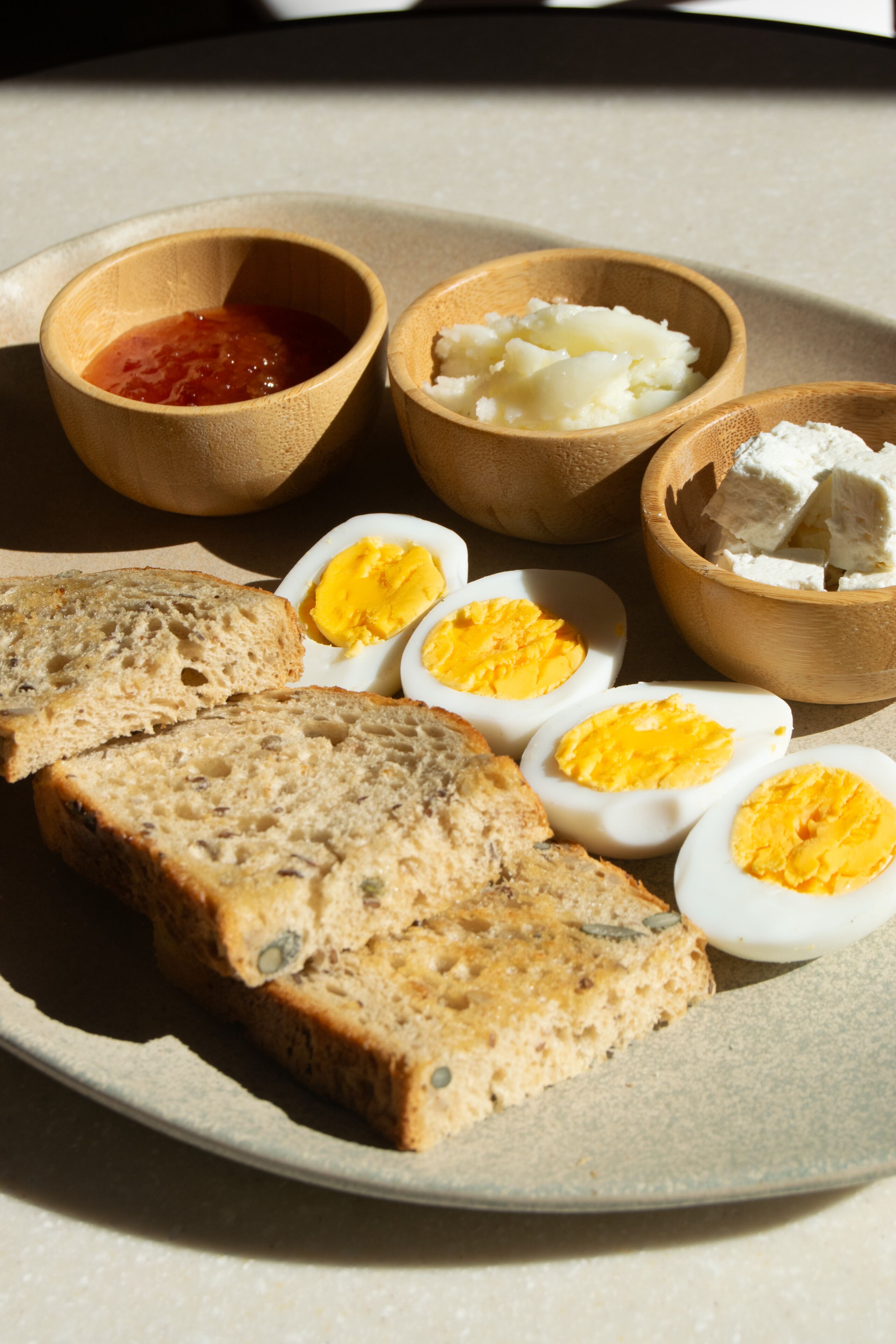 A plate with sliced bread, boiled eggs, and two small bowls containing butter and jam.