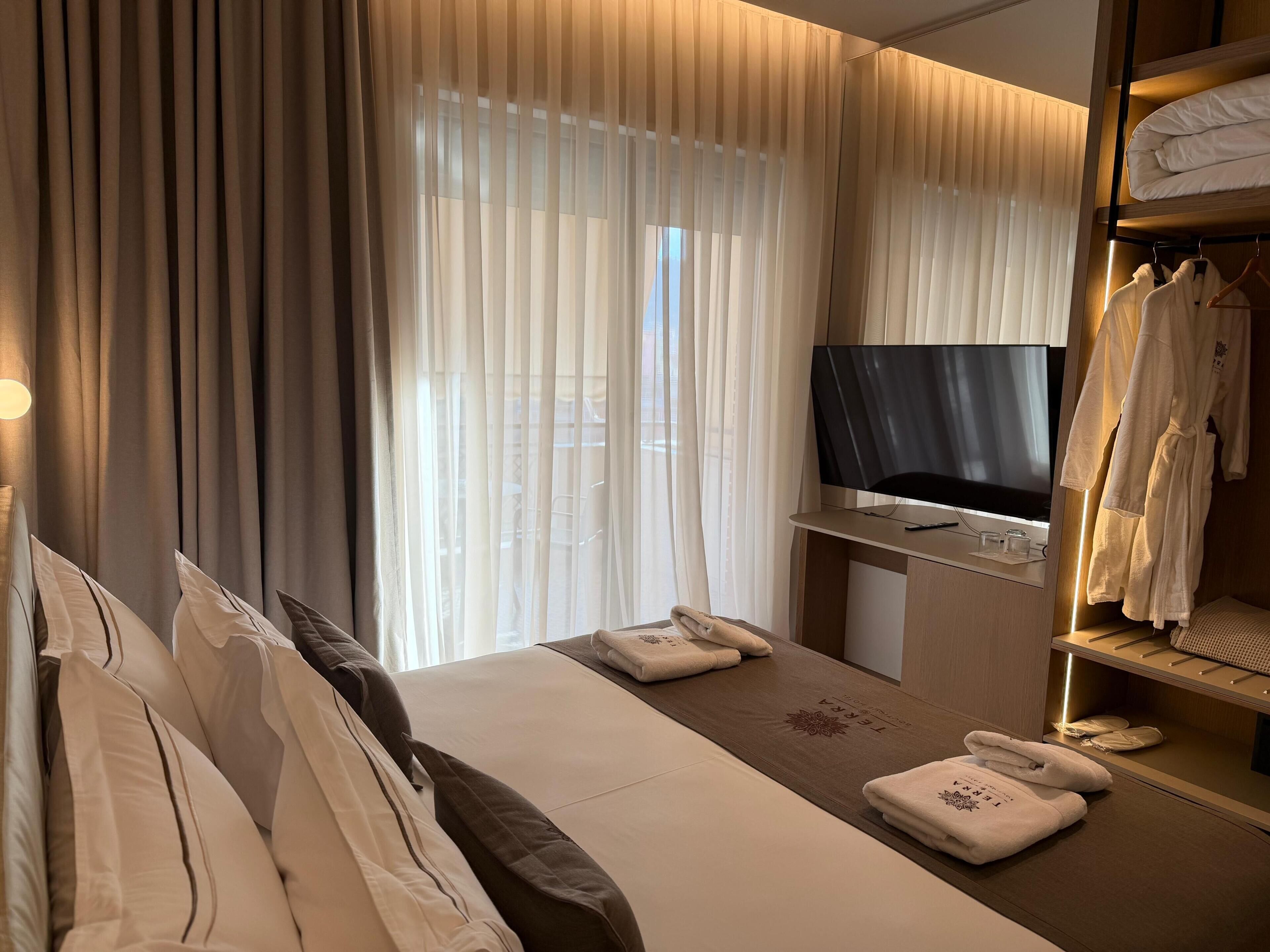 A hotel room with a bed, a TV, a desk with a phone, and a robe rack.