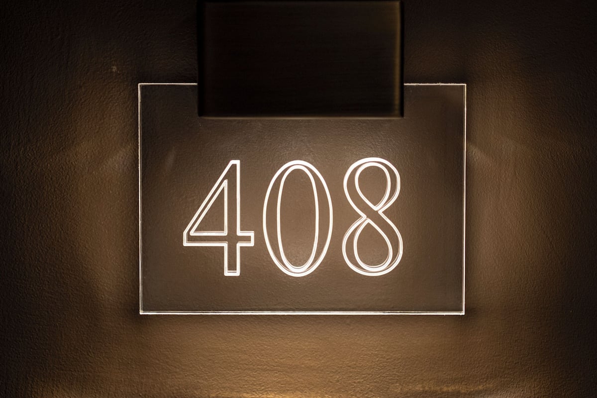 Une plaque rectangulaire fixée au mur, portant le numéro « 408 ».