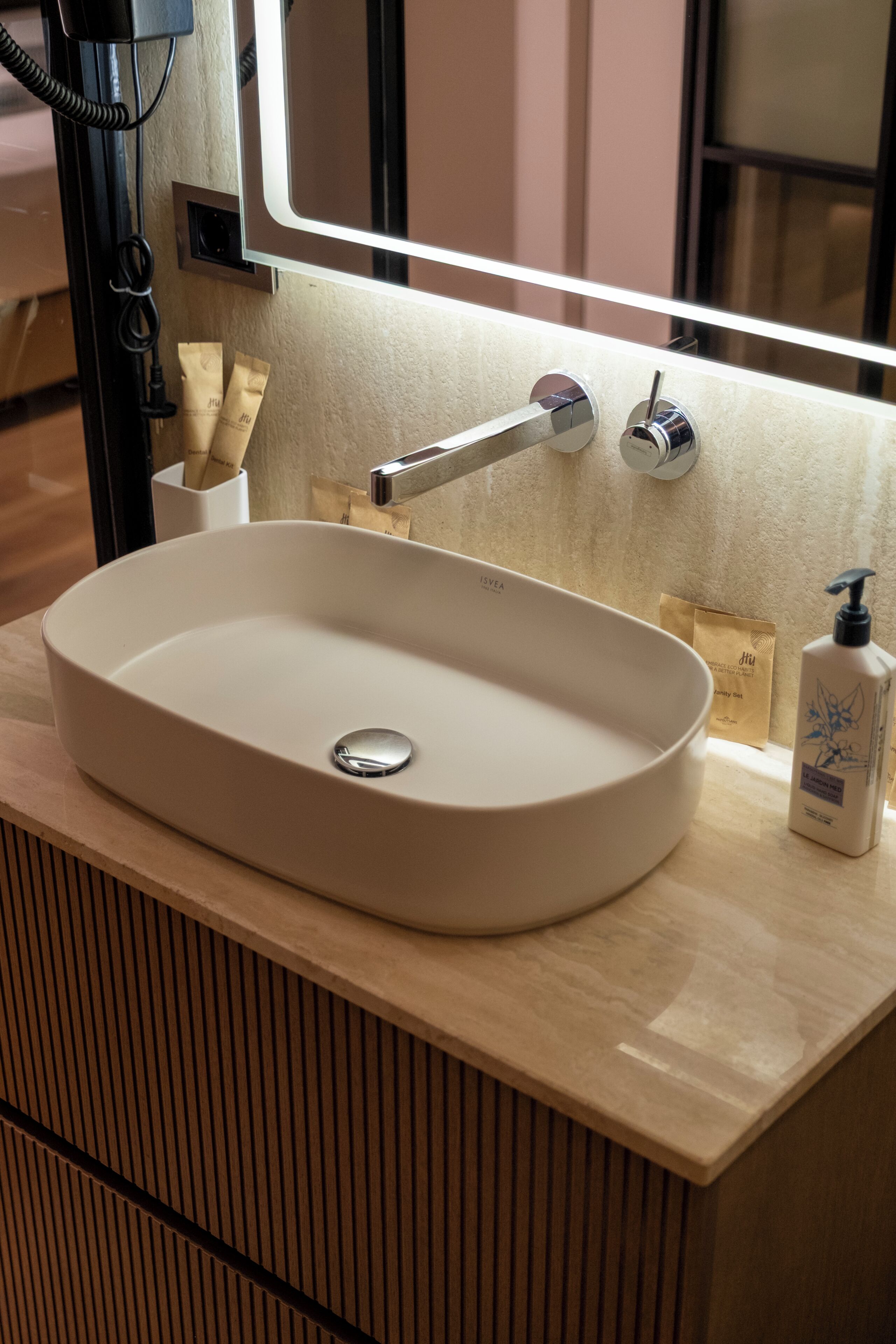 Un baño con un lavamanos blanco, un espejo y una botella de jabón para manos.