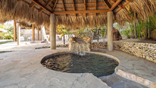 A covered outdoor area with a stone fountain, wooden beams, and a thatched roof. - Beachside 9BR Oasis/Pickle Ball/Infrared Sauna (Sosúa)