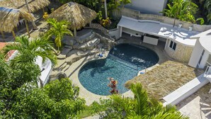 A swimming pool surrounded by thatched-roof structures and lush greenery. - Beachside 9BR Oasis/Pickle Ball/Infrared Sauna (Sosúa)