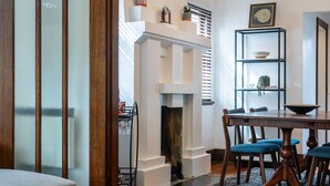 A dining area with a wooden table and blue chairs, a fireplace, and a bookshelf with decorative items. - Pet Friendly - Deco Days in Prahran (Prahran)