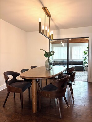 A dining area with a wooden table, six chairs, a vase with a plant, and a modern light fixture.