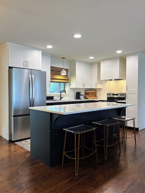 A modern kitchen with a central island, stainless steel appliances, and bar stools.