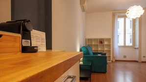 Een moderne keuken met een houten aanrecht, een koffieapparaat en een inbouwoven. Achtergrond toont een teal fauteuil en een witte boekenkast.