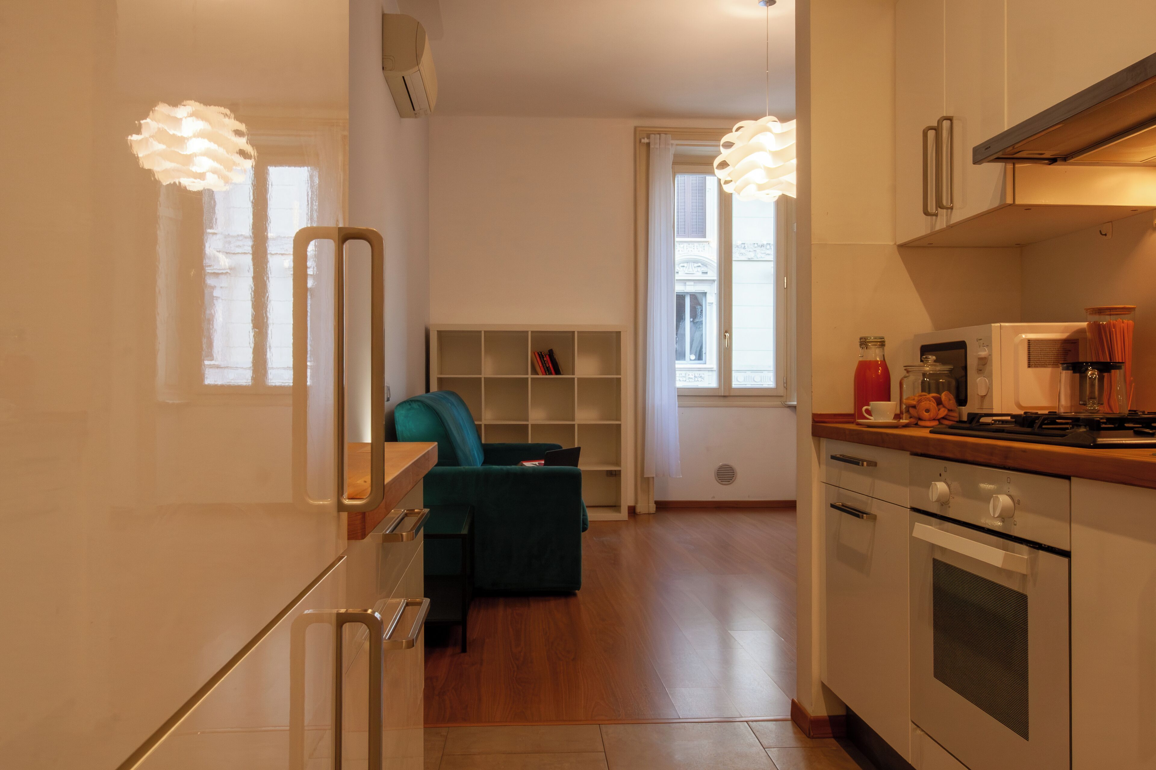 Une cuisine moderne dotée d’un four encastré, un coin repas avec un canapé vert et une bibliothèque.
