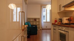 Een moderne keuken met een ingebouwde oven, een eethoek met een groene bank en een boekenkast.