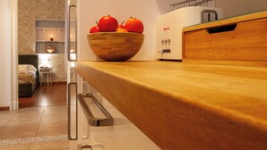 Een keuken met een houten aanrecht, een schaal met fruit, een broodrooster en een kijkje naar een slaapkamer met een bed en nachtkastje.
