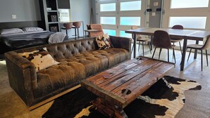 A modern living room with a leather sofa, a wooden coffee table, and a dining area with chairs and a table.