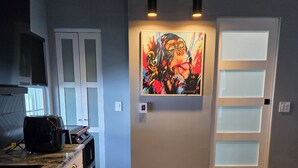 A modern kitchen with a microwave, toaster, and a small table. There is a door with frosted glass panels and a painting above it.