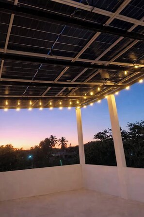 A rooftop terrace with a solar panel roof, white pillars, and string lights.