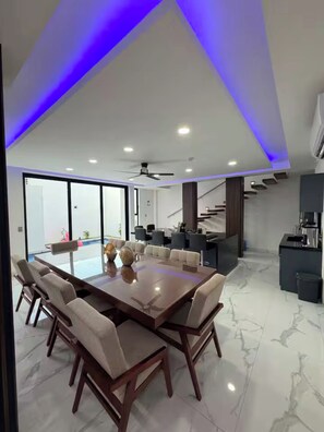 A modern dining area with a large table and chairs, a ceiling fan, and a staircase leading to an upper level.