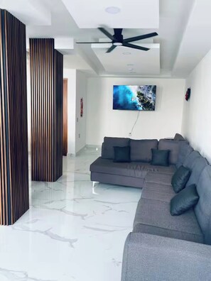 Una sala de estar moderna con un sofá seccional gris, un televisor de pantalla plana montado en la pared y un ventilador de techo.