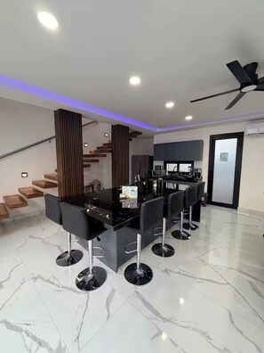 A modern kitchen with a black countertop and bar stools, a staircase with wooden steps, and a ceiling fan.