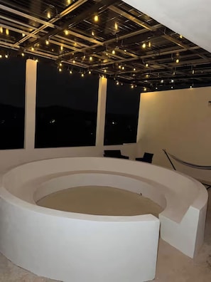 A circular seating area with a white color scheme, surrounded by large windows, and a ceiling with exposed beams and hanging lights.