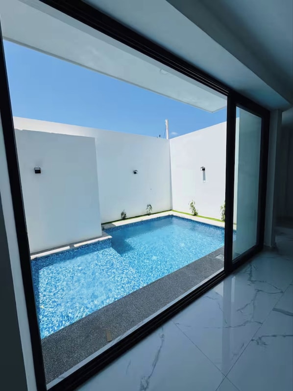 Piscina interior moderna, com água azul cristalina, rodeada por paredes brancas e uma estrutura de vidro.