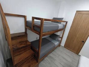 Una cama individual con estructura de madera, ropa de cama gris y una puerta de madera al fondo.