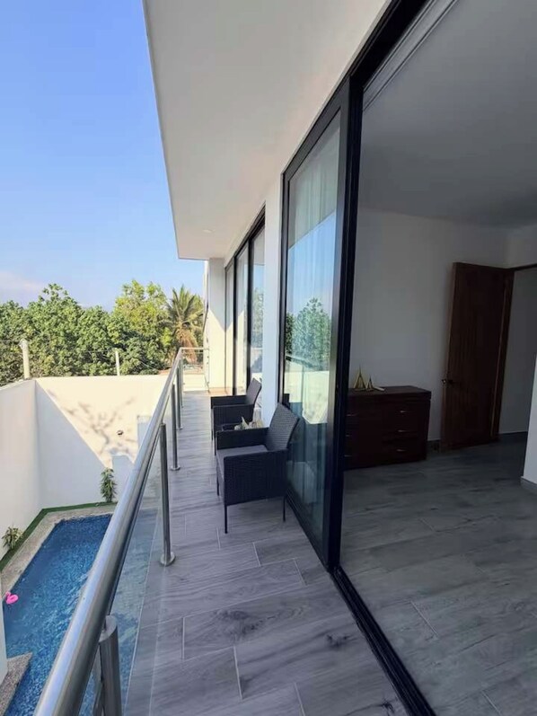 Un balcón moderno con puerta de vidrio, zona de estar con cojines y una piscina pequeña.