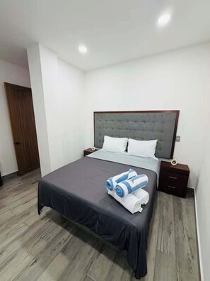 Un dormitorio con cama, mesitas de noche, una puerta de madera y suelo de color claro.