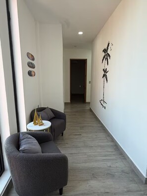 Un pasillo moderno con un sofá gris, una pequeña mesa redonda y decoración en la pared.