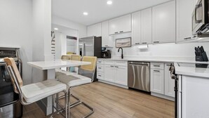 Una cocina moderna con armarios blancos, electrodomésticos de acero inoxidable y una mesa de comedor de madera con taburetes de bar.