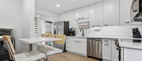 A modern kitchen with white cabinets, stainless steel appliances, and a wooden dining table with bar stools.