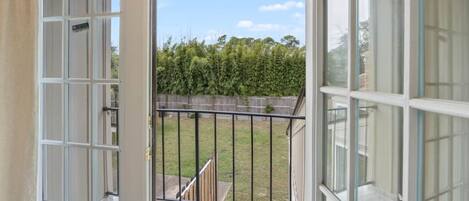 A balcony with a metal railing, a clear view of a green lawn, and a wooden fence in the background.