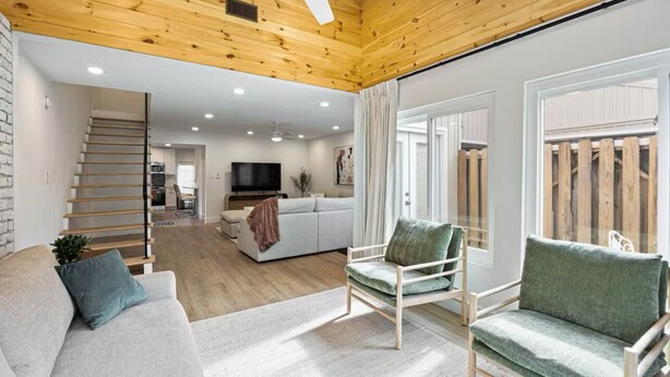 Una sala de estar moderna con techo de madera, un sofá, una silla y un televisor.