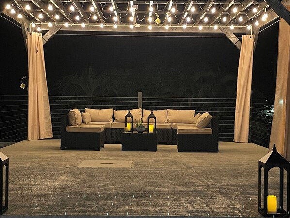 En udendørs siddeplads med sofa, to sofaborde og en pergola med lyskæder.