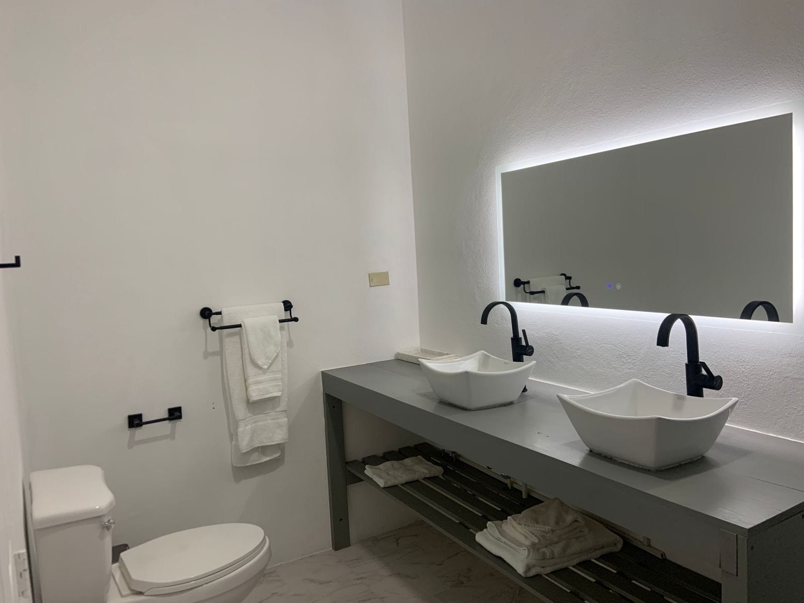 Un baño moderno con dos lavamanos blancos, un espejo grande y un inodoro.