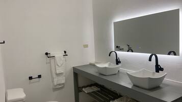 A modern bathroom with two white sinks, a large mirror, and a toilet.