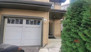 A two-story building with a garage door, a small porch, and a well-maintained hedge. - CozySweetHome (Edmonton)